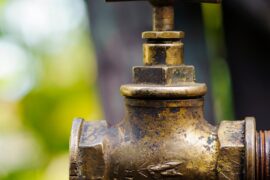 A brass faucet with a valve handle of the same material in an outdoor setting attached to a threaded end.