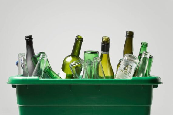 A green, plastic bin contains several empty glass bottles. There are green, clear, and black bottles.