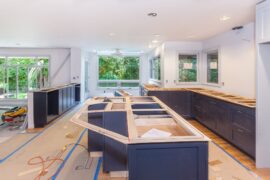 A large kitchen with most of the fixtures and cabinets half finished. There are tools laying on the ground across the kitchen.