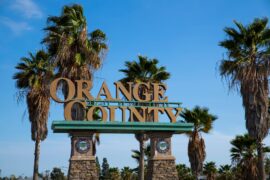 The Orange County public welcome sign on stone pedestals with the seal of the city and palm trees behind it.