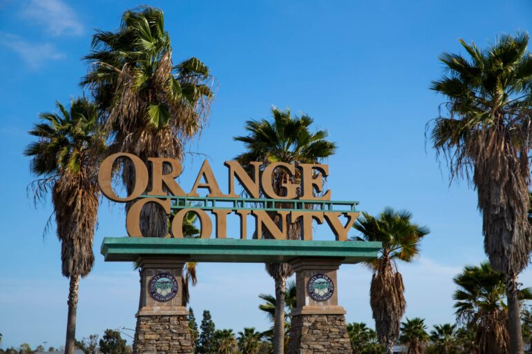 The Orange County public welcome sign on stone pedestals with the seal of the city and palm trees behind it.