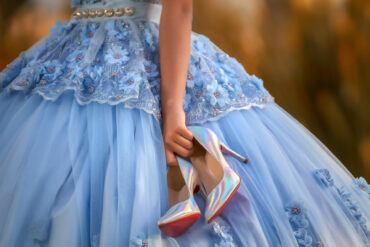 A close-up shows a young girl in a light-blue ballgown with flowers holding a pair of silver holographic heels.