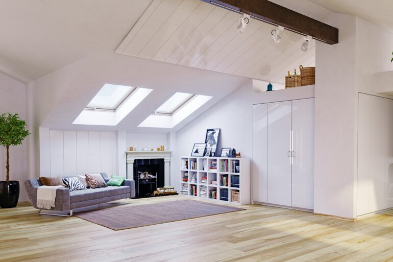 A living room with a slanted ceiling that has two skylights. There’s a couch in the corner that has throw pillows on it.