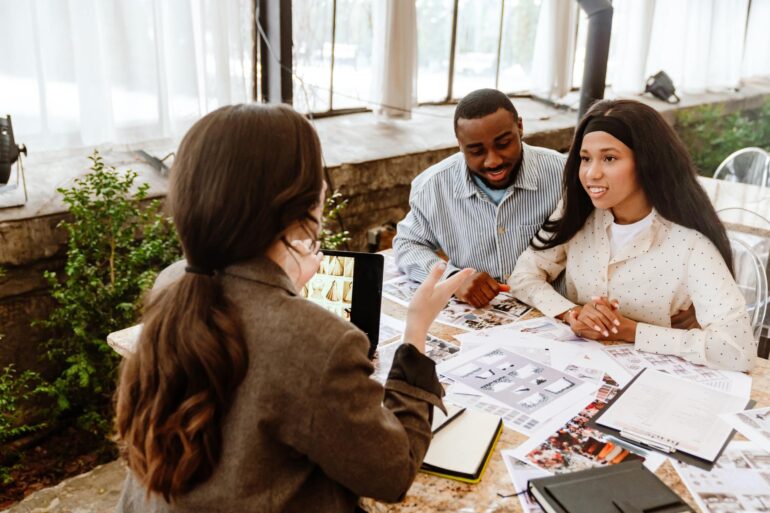 A Black couple faces a brunette woman at a table. They're discussing wedding details.