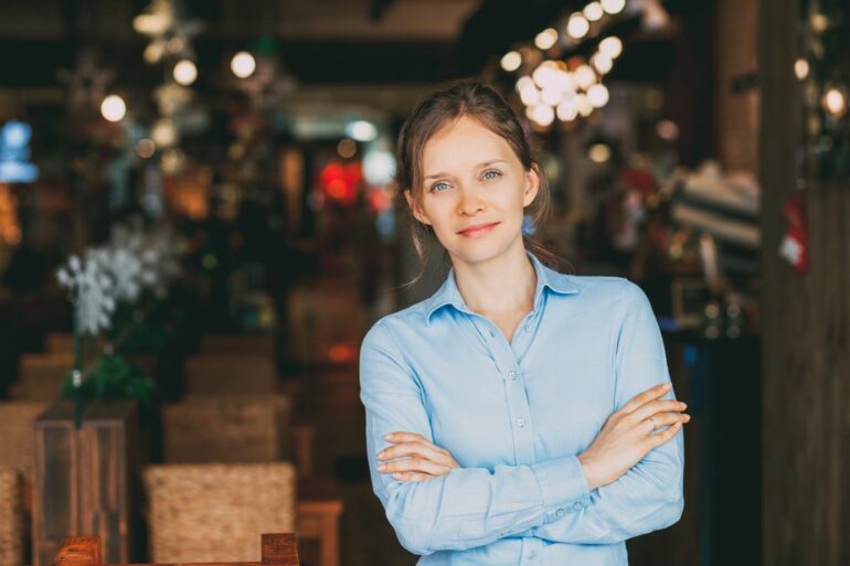 A restaurant manager stands with her arms folded and a confident look on her face in front of her eatery.
