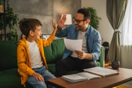 An excited father prepares to high-five his young son after seeing the good grades that he received at school.