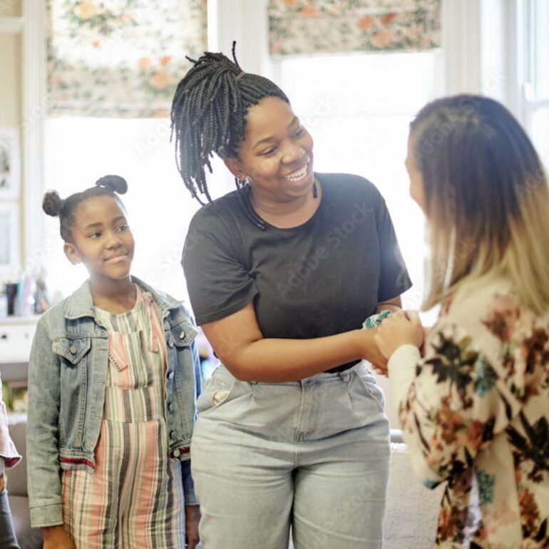 An elementary school teacher warmly greeting the mother of the two students standing behind her.
