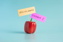 A single red pepper with two small signs attached by toothpicks, reading 'antioxidants' and 'vitamin C.'