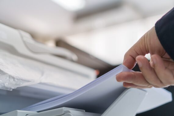 A close-up view shows a person placing a large stack of plain, white paper into the side of a white printer.