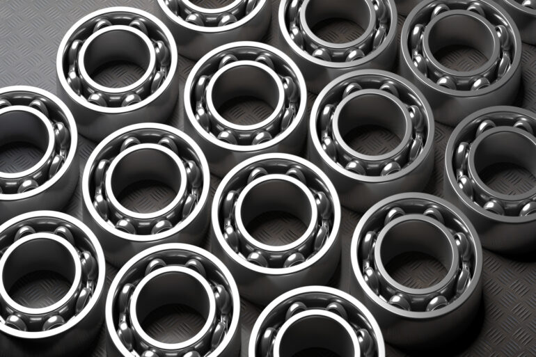 Four rows of bearings lie flat on a dark gray background. The bearings are shiny and made of metal.