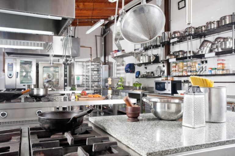 A well-organized restaurant kitchen with various appliances on the clean counter, including a bowl and grater.