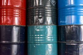 Three industrial drums have another industrial drum stacked on top of them. They are black, green, red, and blue.