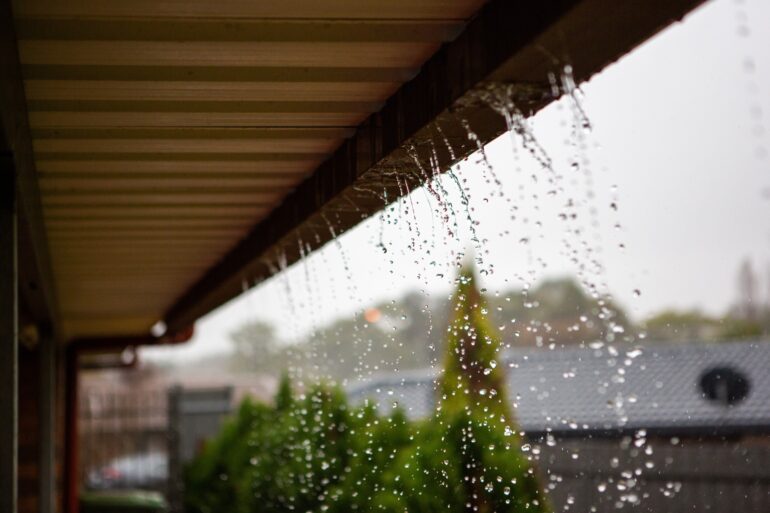A close-up of a home's gutters under the overhand. There is water flowing from the gutters signaling a clog.
