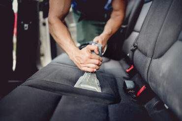 A person deep cleaning the back of a car with a water vacuum. The nozzle is pressed against the seats and has dirty water.