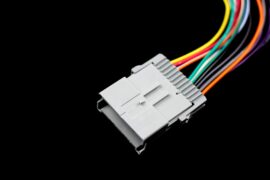 A close-up of an automotive electrical connector against a black background. The connector has multicolored wires.