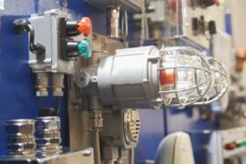An industrial gas leak control panel and fire alarm light with a protective cage mounted on equipment in a manufacturing facility.