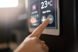 A person is pressing their finger against a touch screen. On the screen is a thermostat with a temperature reading.
