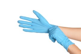 A close-up of a person stretching a blue disposable glove over their hand, adjusting the fit against a light background.