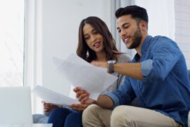 A couple reviews financial paperwork together at a table, smiling while discussing bills, budget, and household finances.