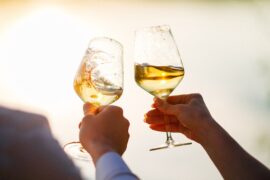 A close-up view shows two people raising wine glasses filled with white wine up into the air to toast.