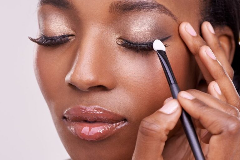 Close-up of person applying eyeshadow with brush to closed eyelid, showing smooth skin and blended makeup detail.
