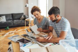 A couple sitting in their living room, looking at a book of various materials for a home renovation project.
