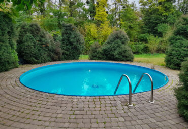 A close-up of a circular swimming pool lined by several rows of bricks and some small trees. There is a ladder in the pool.