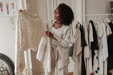 Individual holds textured white sweater on hanger near clothing rack with minimalist outfits in softly lit interior.