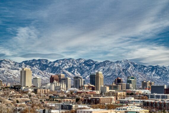 A landscape view of the skyline of Salt Lake City, including skyscrapers and snow-capped mountains behind them.