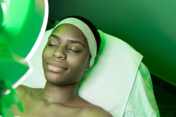 A Black woman laying back on a medical table while resting her head against a white towel during a skin treatment.