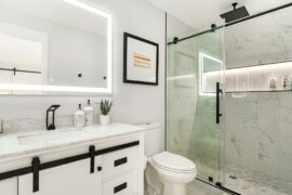 A modern bathroom with white cabinets, black hardware, a walk-in shower with large glass doors next to a toilet.