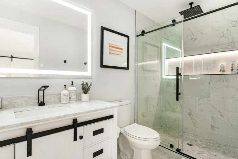 A modern bathroom with white cabinets, black hardware, a walk-in shower with large glass doors next to a toilet.
