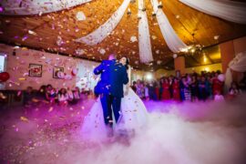 A bride and groom dancing together on a dance floor. A group of wedding guests is encircling the couple.