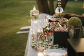 An outdoor catering table with an assortment of hors d'oeuvres. Some of the food is on trays and some is in small cups.