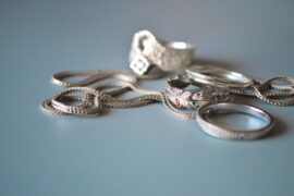 A braided silver chain and several silver rings with textured details resting on a soft blue surface.