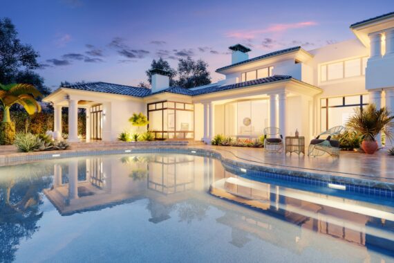 Luxury home with illuminated backyard swimming pool at dusk, surrounded by a spacious patio, columns, and landscaping.