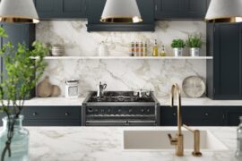 A modern kitchen with a granite island counter and a backsplash, a stainless-steel oven, and grey cabinets.